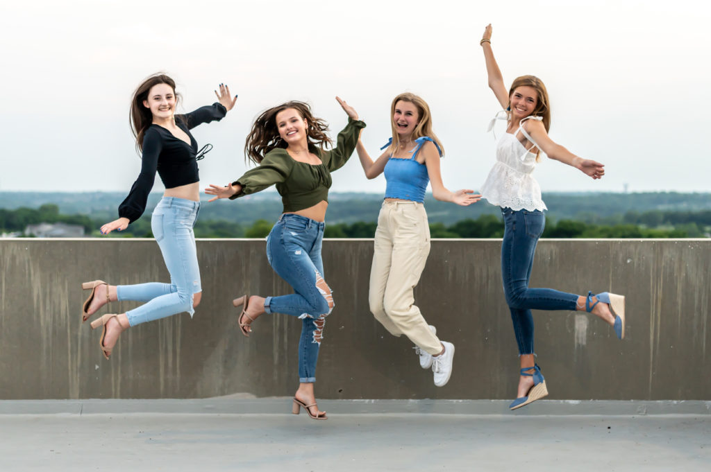 four high school senior girls jumping with hands in the air to celebrate 